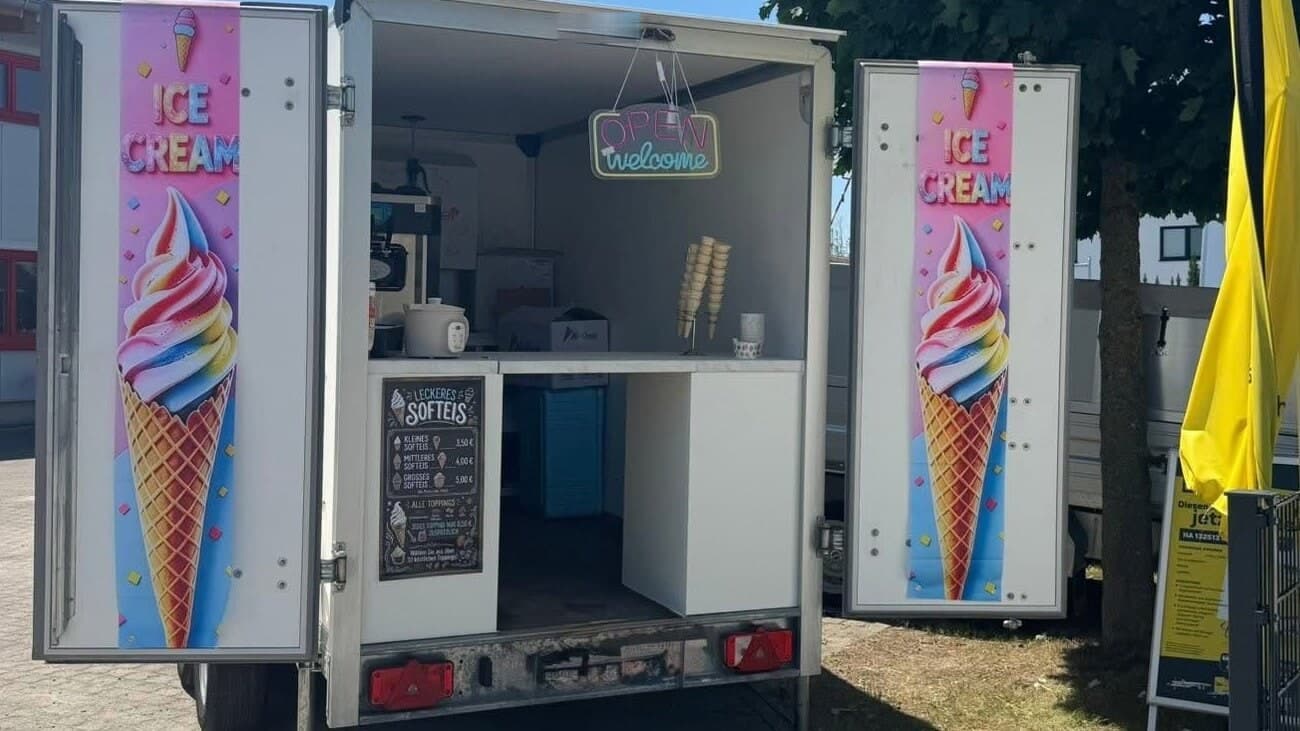 Der geöffnete Softeis-Anhänger von Mondy Softeis an einem sonnigen Nachmittag auf dem Platz, beide Klappen offen