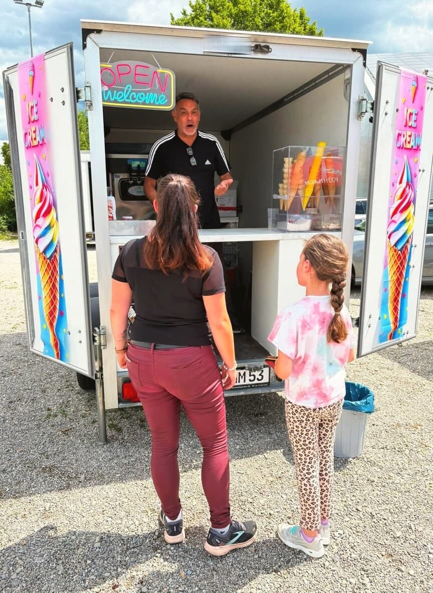 Mondy reicht an der Theke des geöffneten Softeis-Wagens eine Waffel heraus