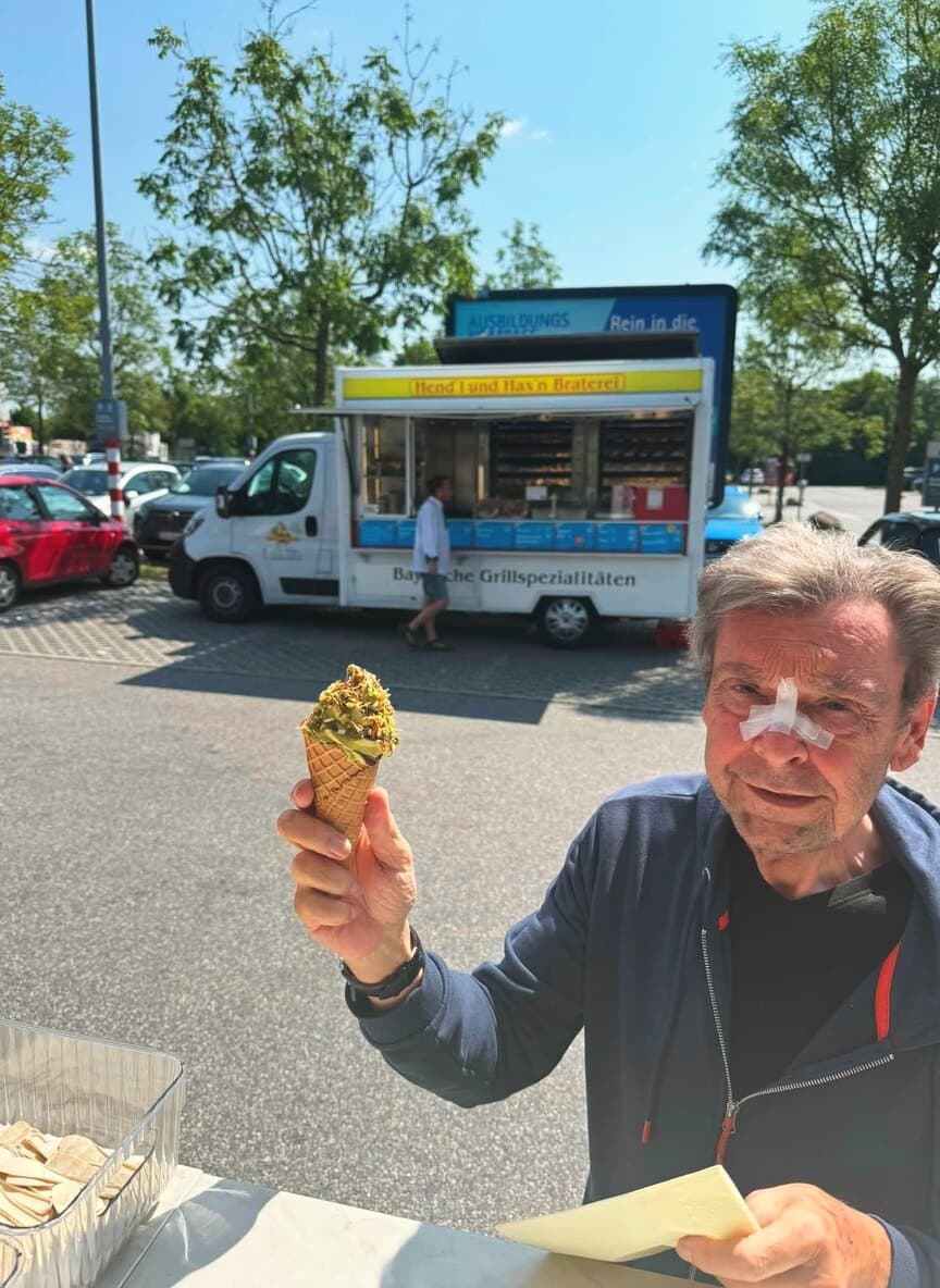 Gast hält ein Softeis mit Pistazienkrokant am Wagen in die Kamera